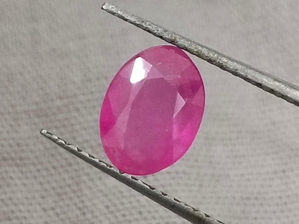 GSI Certified 1.31ct natural untreated pinkish red African ruby gemstone held with tweezers.