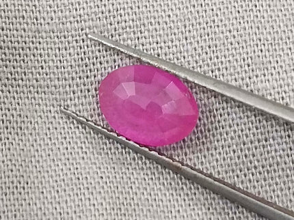 Natural untreated pinkish red African ruby gemstone, oval shape, good clarity, displayed with tweezers.