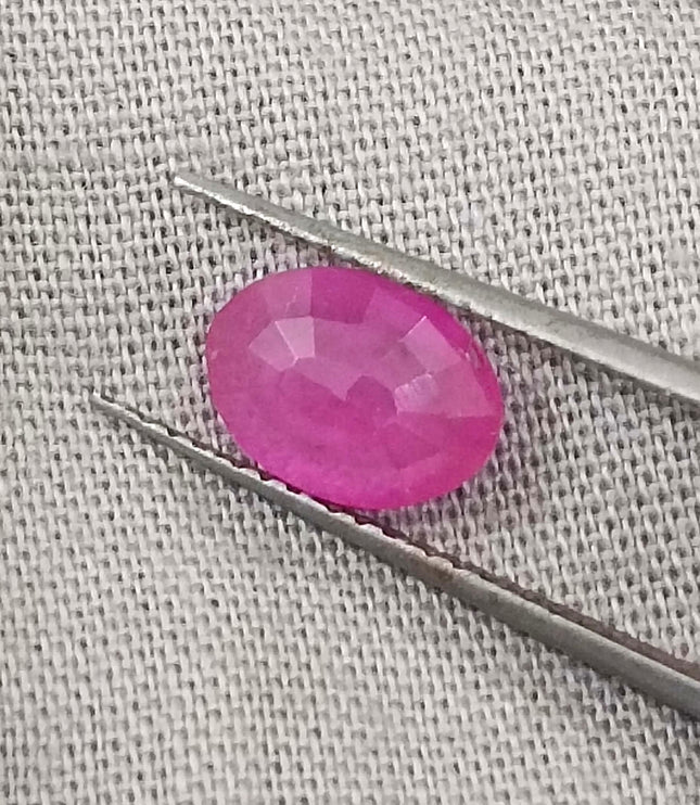 Natural untreated pinkish red African ruby gemstone, oval shape, good clarity, displayed with tweezers.