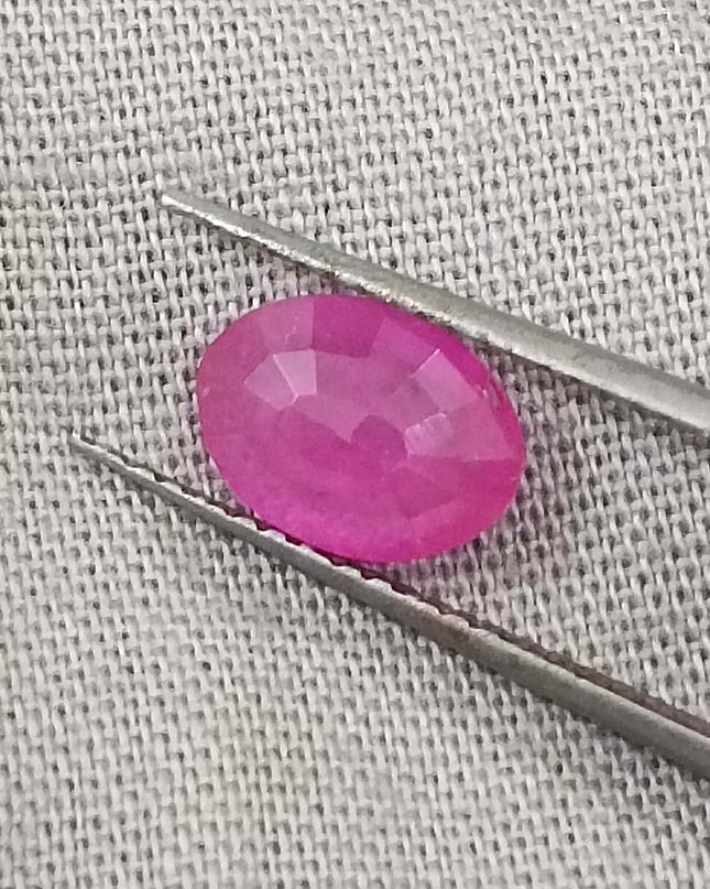 Natural untreated pinkish red African ruby gemstone, oval shape, good clarity, displayed with tweezers.