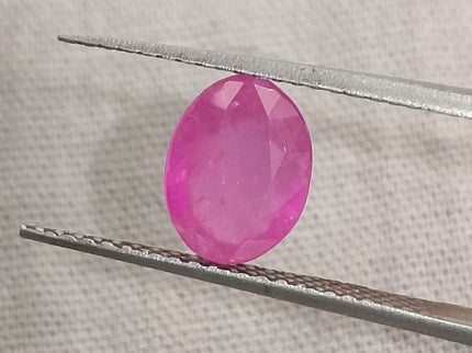Natural untreated oval pinkish red African ruby gemstone held by tweezers, GSI certified, 1.31ct.
