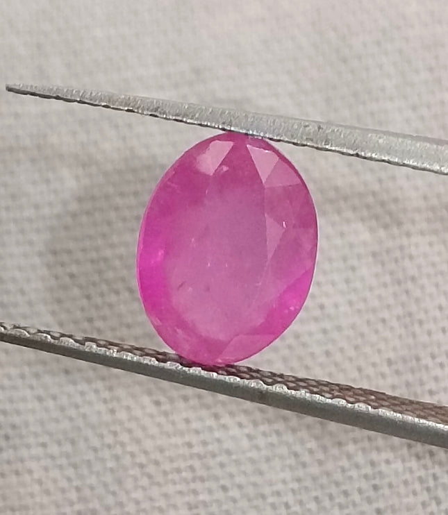 Natural untreated oval pinkish red African ruby gemstone held by tweezers, GSI certified, 1.31ct.