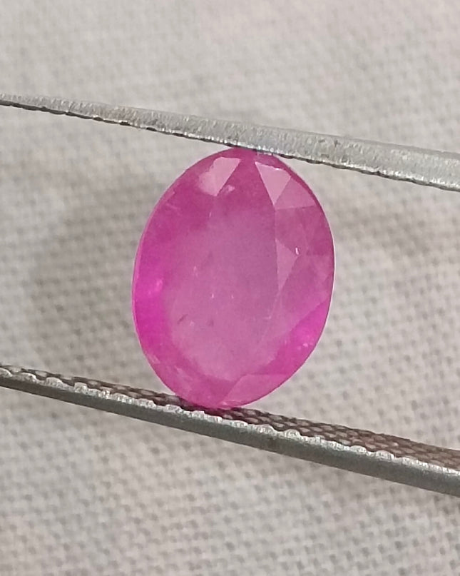 Natural untreated oval pinkish red African ruby gemstone held by tweezers, GSI certified, 1.31ct.
