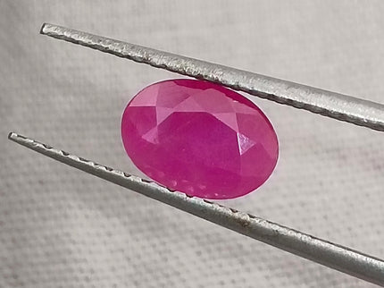 Natural untreated oval ruby held by tweezers, showcasing deep red color, good clarity, and cut quality.