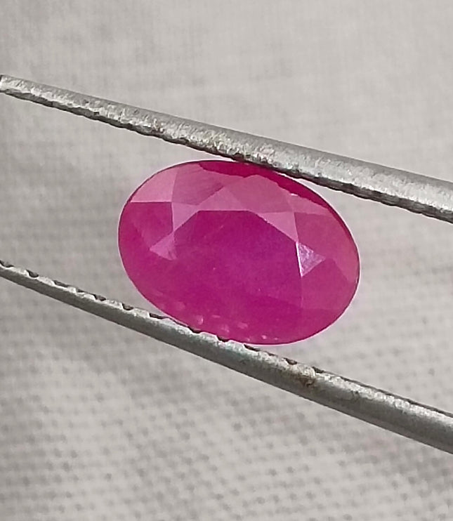 Natural untreated oval ruby held by tweezers, showcasing deep red color, good clarity, and cut quality.