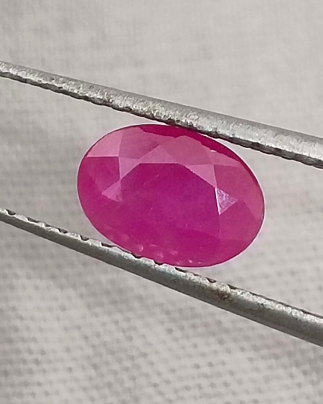 Natural untreated oval ruby held by tweezers, showcasing deep red color, good clarity, and cut quality.