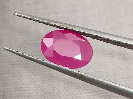 Natural untreated oval pink ruby gemstone displayed with tweezers, showcasing its vibrant color and quality cut.