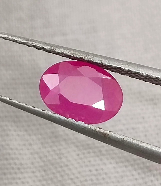 Natural untreated oval pink ruby gemstone displayed with tweezers, showcasing its vibrant color and quality cut.