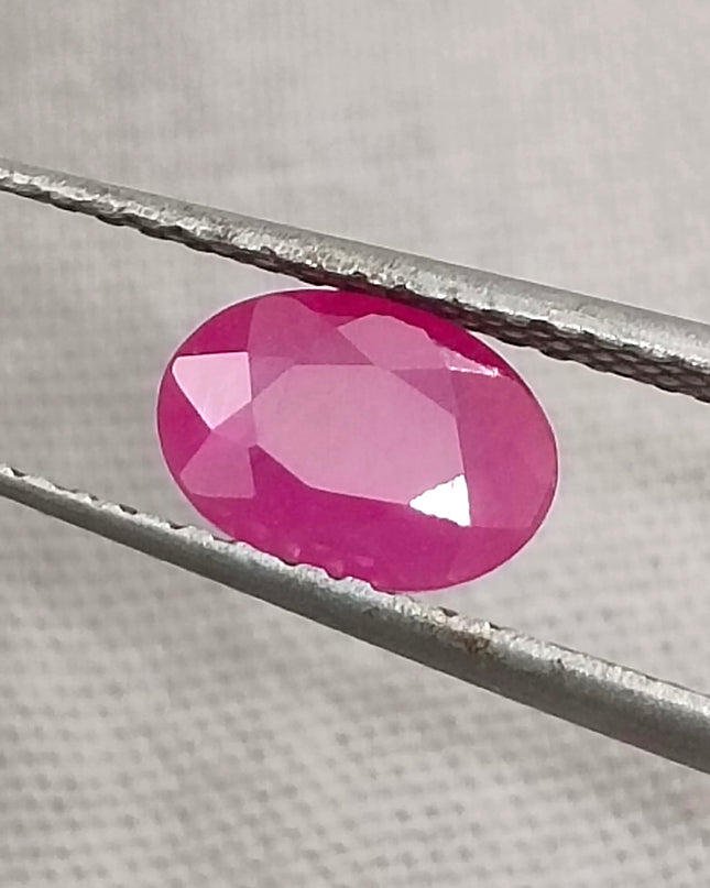Natural untreated oval pink ruby gemstone displayed with tweezers, showcasing its vibrant color and quality cut.